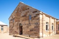 Sandstone brick built building with decorative stonework and doorway set in pebbled courtyard against clear blue sky