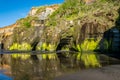 Sandstone cliff formation reflecting in the water at the Three Sisters beach on the Tasman Sea shores of Taranaki, New Zealand