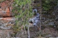 Sandstone cliff pattern with orange clay rock and green trees in the foreground. Water icicles are frozen in the rock