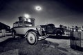 Old vintage vehicles park under a full moon at Sandstone Estates in black and white