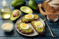 Sandwich with avocado puree and egg on a plate and ingredients for cooking on a blue wooden table Royalty Free Stock Photo