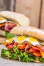 A sandwich with bacon, cheese and fried quail eggs. A sandwich with fresh vegetables and herbs on a wooden background. Royalty Free Stock Photo