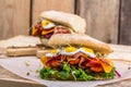 A sandwich with bacon, cheese and fried quail eggs. A sandwich with fresh vegetables and herbs on a wooden background. Royalty Free Stock Photo