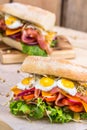 A sandwich with bacon, cheese and fried quail eggs. A sandwich with fresh vegetables and herbs on a wooden background. Royalty Free Stock Photo