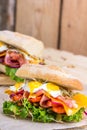 A sandwich with bacon, cheese and fried quail eggs. A sandwich with fresh vegetables and herbs on a wooden background. Royalty Free Stock Photo