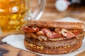 Sandwich with beef, fried onion, cheese and bacon with granular mustard. Beer and snack on the table Royalty Free Stock Photo