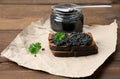 Sandwich with black caviar on a slice of rye bread and a jar with a spoon, a delicious snack on the table