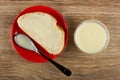 Sandwich with condensed milk, spoon in red saucer, transparent bowl with milk on wooden table. Top view Royalty Free Stock Photo
