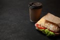 Sandwich and cup of coffee on black background. Morning breakfast or snack when hungry. Street food to go. Copy space for text.