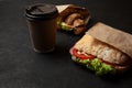 Sandwich and cup of coffee on black background. Morning breakfast or snack when hungry. Street food to go Royalty Free Stock Photo