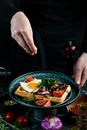 Sandwich with egg, tomatoes and bacon on a plate in the hands of a chef On a black background. Royalty Free Stock Photo