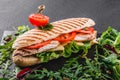 Sandwich with fillet grilled chicken, fresh vegetables, cheese and greens on black shale board over black stone background Royalty Free Stock Photo