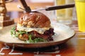 Sandwich with pastrami, vegetables, mimolette cheese, with a sweet roll, on a plate, on a wooden table, side view. Royalty Free Stock Photo