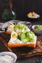 Sandwich with ricotta, cucumber slices, boiled egg and sesame seeds on a board vertical view