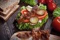 Sandwich with smoked meat, green salad, fresh tomatoes and pickled cucumbers, on kitchen wooden table background Royalty Free Stock Photo