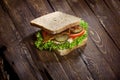 Sandwich with smoked meat, green salad, fresh tomatoes and pickled cucumbers, on kitchen wooden table background Royalty Free Stock Photo