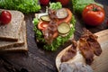 Sandwich with smoked meat, green salad, fresh tomatoes and pickled cucumbers, on kitchen wooden table background Royalty Free Stock Photo