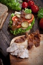 Sandwich with smoked meat, green salad, fresh tomatoes and pickled cucumbers, on kitchen wooden table background Royalty Free Stock Photo