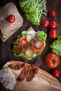 Sandwich with smoked meat, green salad, fresh tomatoes and pickled cucumbers, on kitchen wooden table background Royalty Free Stock Photo