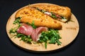 Sandwich with smoked pork ham, mozzarella, tomatoes and arugula salad on wooden plate on black background Royalty Free Stock Photo