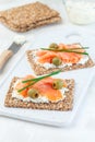 Sandwich with smoked salmon and cream cheese on thin multi seed crispbread, garnished with green onion and olives, vertical