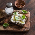 Sandwich with soft cheese, olive oil and basil, served on olive cutting board on dark wooden surface. Royalty Free Stock Photo