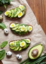 Sandwich, toast with avocado, spinach, guacamole and quail eggs on parchment and dark wooden table.