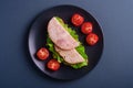 Sandwich with turkey ham meat, green salad and fresh cherry tomatoes slices on black plate, blue minimal background Royalty Free Stock Photo