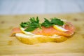 Sandwich of white bread with butter, lightly salted salmon, lemon slices and herbs on the background of a yellow cutting board. Royalty Free Stock Photo