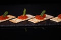 Sandwiches of cracker canapes with red caviar and butter and a leaf of green mint on a plate of slate. Seafood, red caviar.