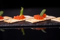 Sandwiches of cracker canapes with red caviar and butter and a leaf of green mint on a plate of slate. Seafood, red caviar.