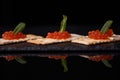 Sandwiches of cracker canapes with red caviar and butter and a leaf of green mint on a plate of slate. Seafood, red caviar.