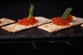 Sandwiches of cracker canapes with red caviar and butter and a leaf of green mint on a plate of slate. Seafood, red caviar.