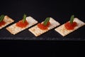 Sandwiches of cracker canapes with red caviar and butter and a leaf of green mint on a plate of slate. Seafood, red caviar.