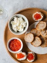 Sandwiches with cream cheese and red caviar on large wooden tray and ingredients in bowls. Top view