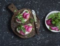 Sandwiches with feta cheese, radishes, arugula on rustic cutting board on a dark background.