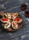 Sandwiches with goat cheese, anchovies, roasted peppers, ham and two glasses of red wine on a wooden rustic board. Royalty Free Stock Photo