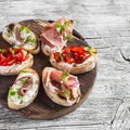 Sandwiches with goat cheese, anchovies, roasted peppers, ham on a wooden rustic board.