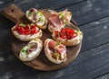 Sandwiches with goat cheese, anchovies, roasted peppers, ham on a wooden rustic board.