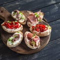 Sandwiches with goat cheese, anchovies, roasted peppers, ham on a wooden rustic board.