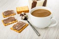 Sandwiches with chocolate-dairy paste, spoon and jar with paste, cup of coffee with milk on wooden table