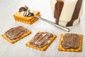 Crackers with chocolate-dairy paste, spoon and jar with paste, few cookies on wooden table