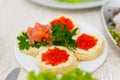 Sandwiches with red caviar and salmon are spread on a plate on a buffet table close up.