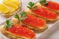Sandwiches with red caviar on a white plate. Gourmet appetizer of trout caviar on a slice of french baguette with butter. Salted