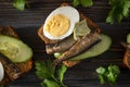 Sandwiches with sprats, fresh cucumber, parsley, rye bread and egg on a dark wooden background