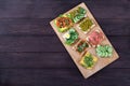 Sandwiches on toast bread with cream cheese with salmon, sprouts, vegetables lie on a wooden board on a brown wooden background.