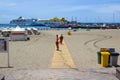 The sandy bay at and ferry terminal at Los Cristianos in Tenerife with island ferries in port and holiday makers walking the beach