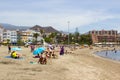The sandy bay at Los Cristianos in Tenerife with holiday makers sun bathing and hotels and mountains in the background