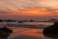 Sandy beach with large stones against the backdrop of sea waves under a bright orange purple sunset sky Royalty Free Stock Photo