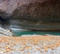 Sandy beach of the mountain river covered with fallen yellow autumn leaves and a man traveler sitting on a rocky shore Royalty Free Stock Photo